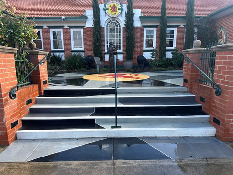 Glass gates and black steps leading to a brick building with red tile roof, ivy vines, and cypress trees