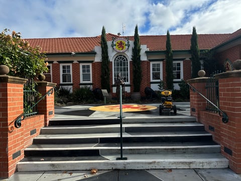 Red brick building with pitched roof, tall cypress trees, and metal entry gates leading to a courtyard