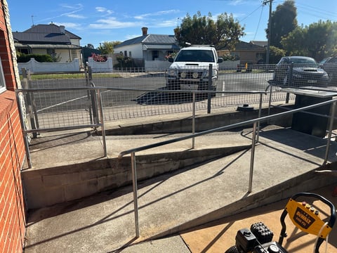 Metal gate and fence framework under construction in a residential driveway with vehicles and houses visible in background