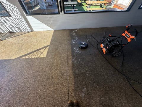 Orange and black drone sitting on dark floor next to controller, viewed from above in an indoor space with windows