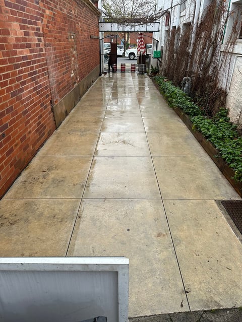 Narrow wet concrete alleyway between brick and weathered walls, leading to a storefront in the distance